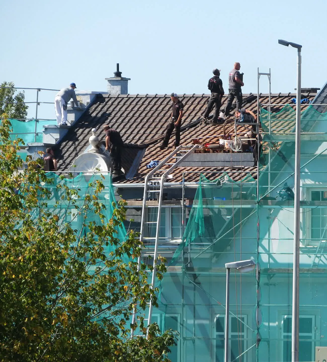 Couvreurs posant et alignant des tuiles sur la toiture d'un immeuble en rénovation, le long d'un échafaudage