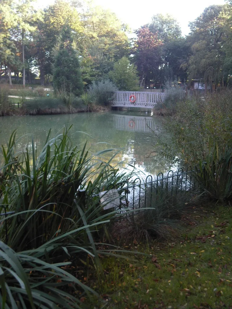 Le bassin du parc de Ladoucette à Drancy, entouré de saules et de massifs, avec sa passerelle en bois