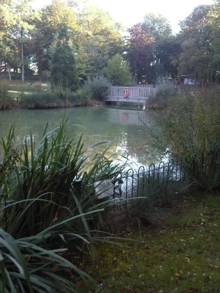 Le bassin du parc de Ladoucette à Drancy, entouré de saules et de massifs, avec sa passerelle en bois